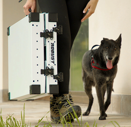 Hunter carrying a folded white Robust dog crate with a black dog at their side.