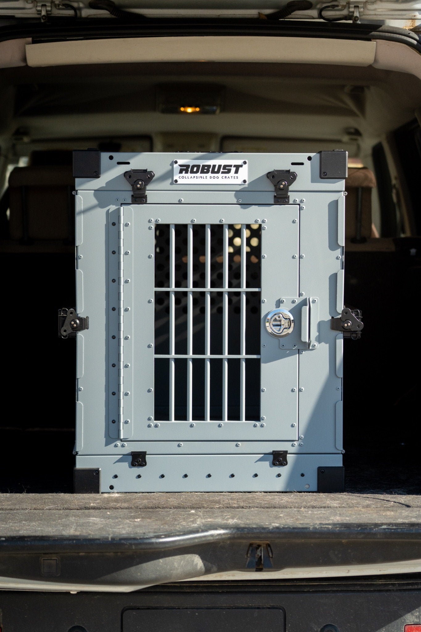 Front view of the grey Robust collapsible dog crate installed in the boot of a car.