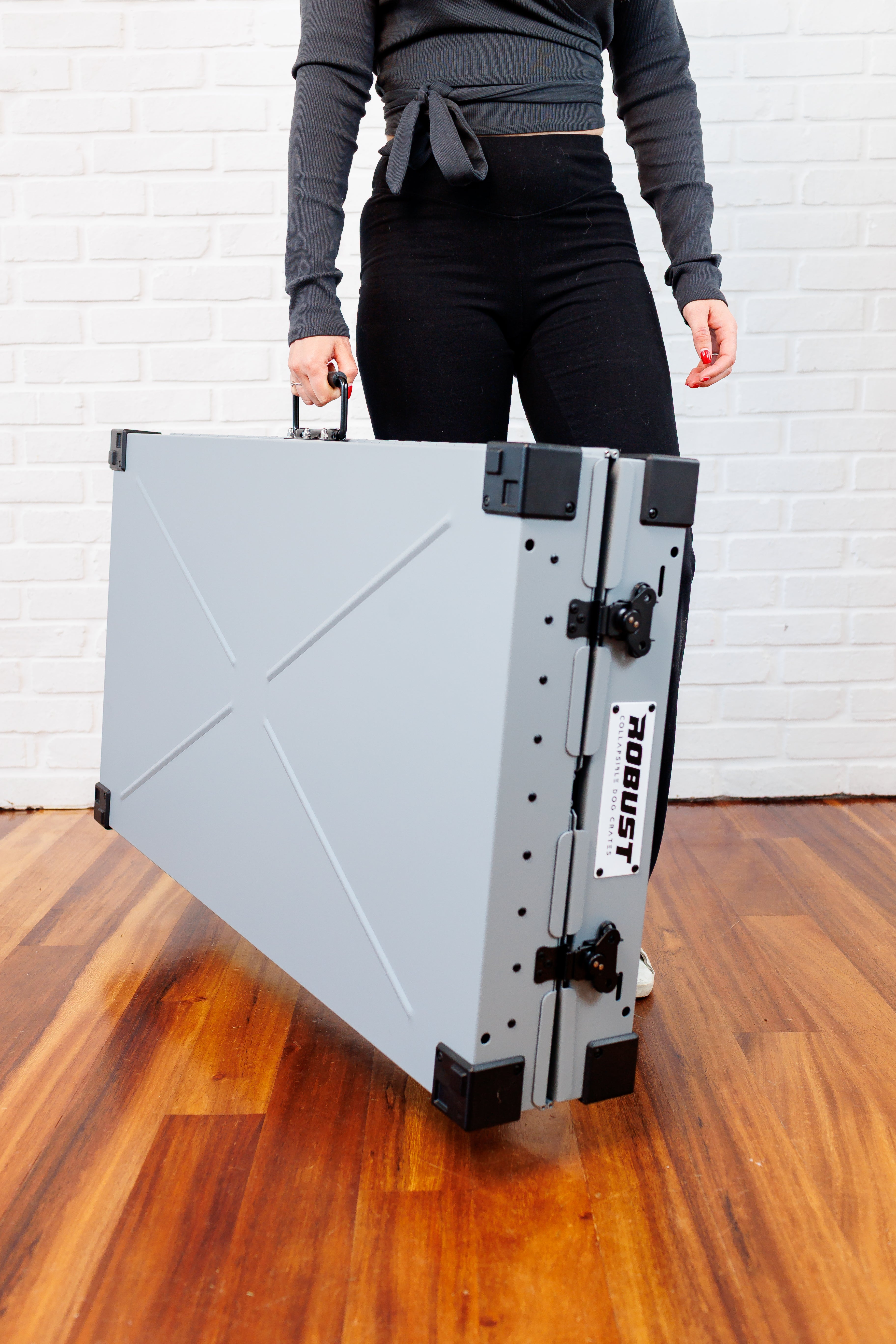 Person carrying the grey Robust collapsible dog crate folded flat by its handle.