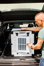 Person securing a white Robust collapsible dog crate in the boot of a car.