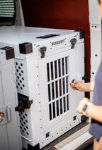 Person securing the door lock of a white Robust collapsible dog crate inside a van
