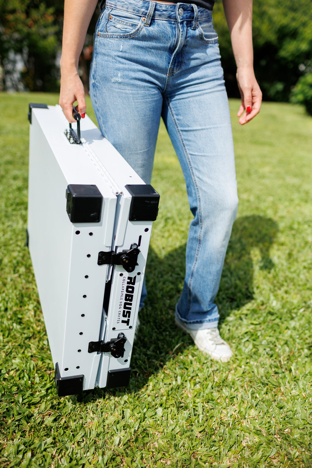 Close-up of a person carrying a folded white Robust collapsible dog crate by its handle.