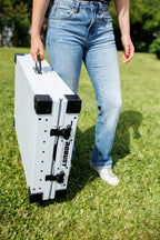 Close-up of a person carrying a folded white Robust collapsible dog crate by its handle.